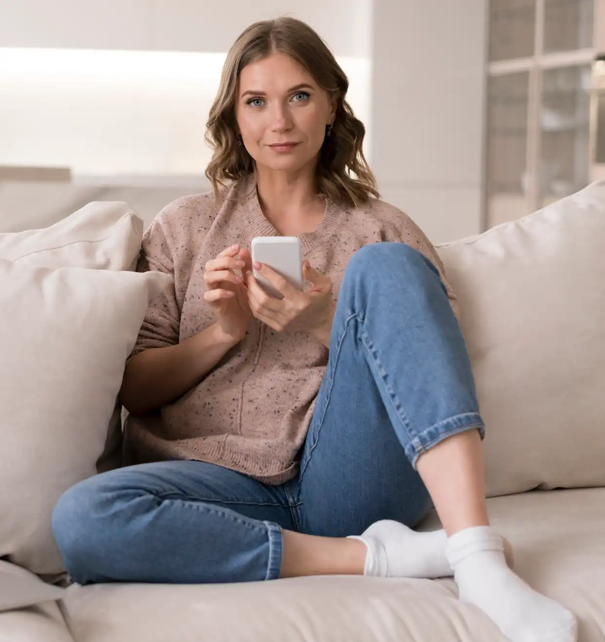 Depilación láser y tratamientos estéticos Mujer joven sentada en el sofá contactando con Dpila y estética desde el móvil y sonriendo